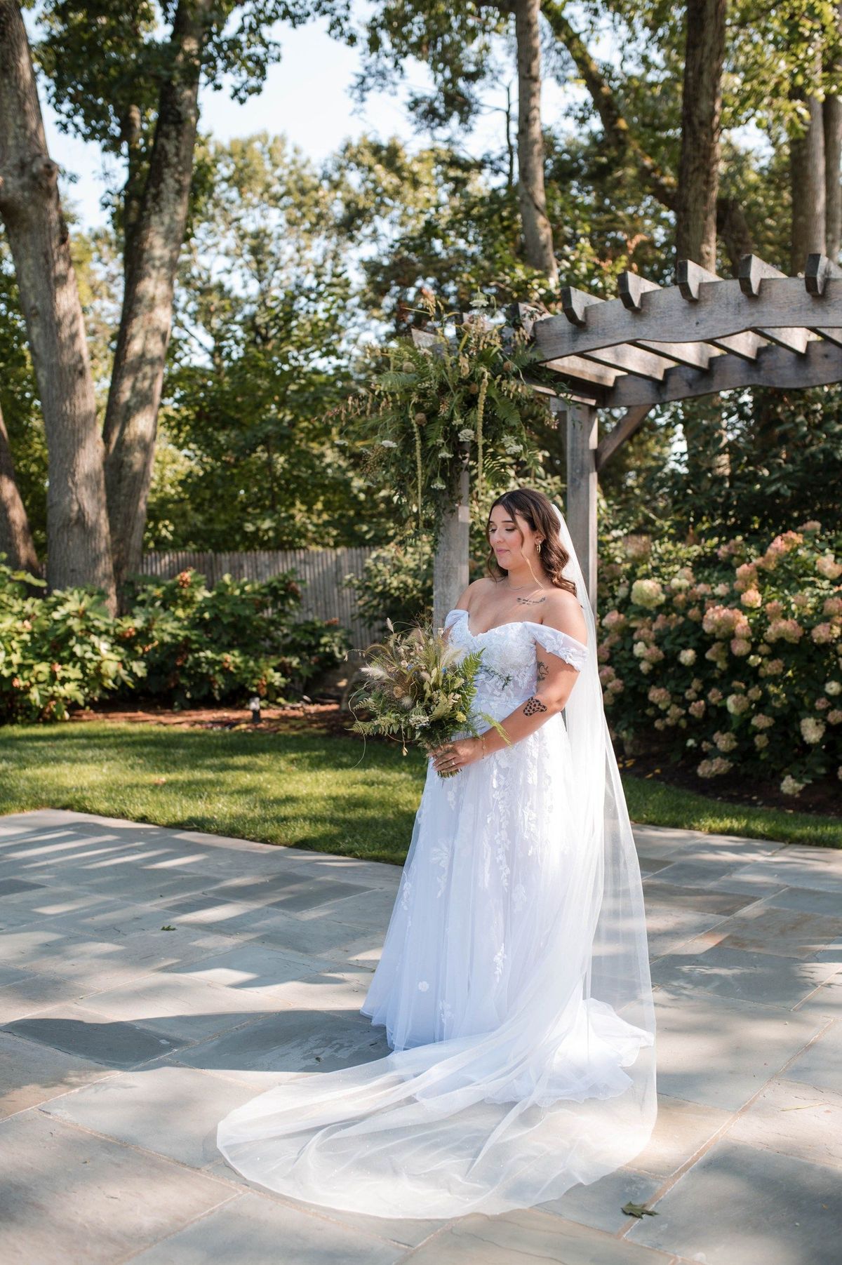 Sophia holds her bouquet in a full-length bridal portrait beneath the arbor