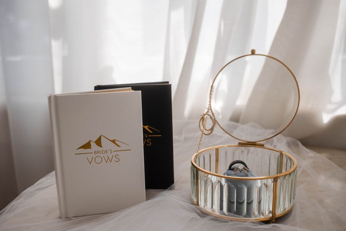 Vow books and a ring box rest beside a window before the wedding
