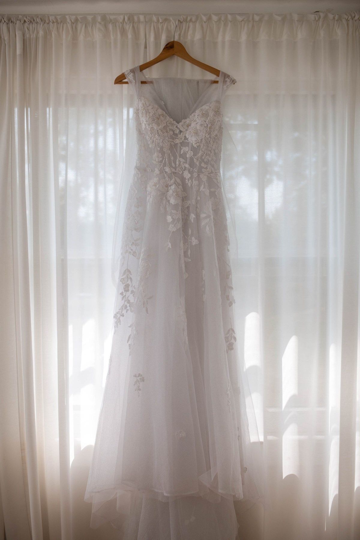 Sophia’s wedding dress hangs in front of sheer window curtains