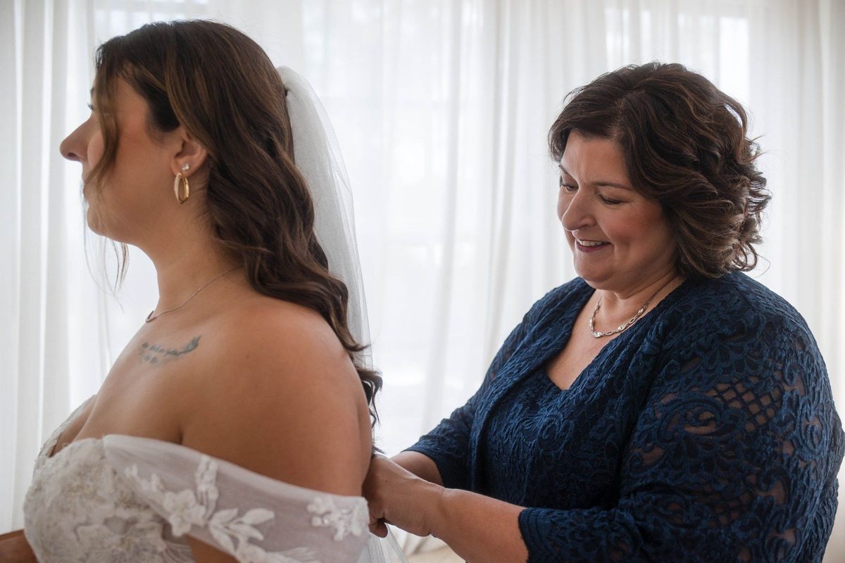 A woman helps fasten Sophia’s wedding dress by a bright window