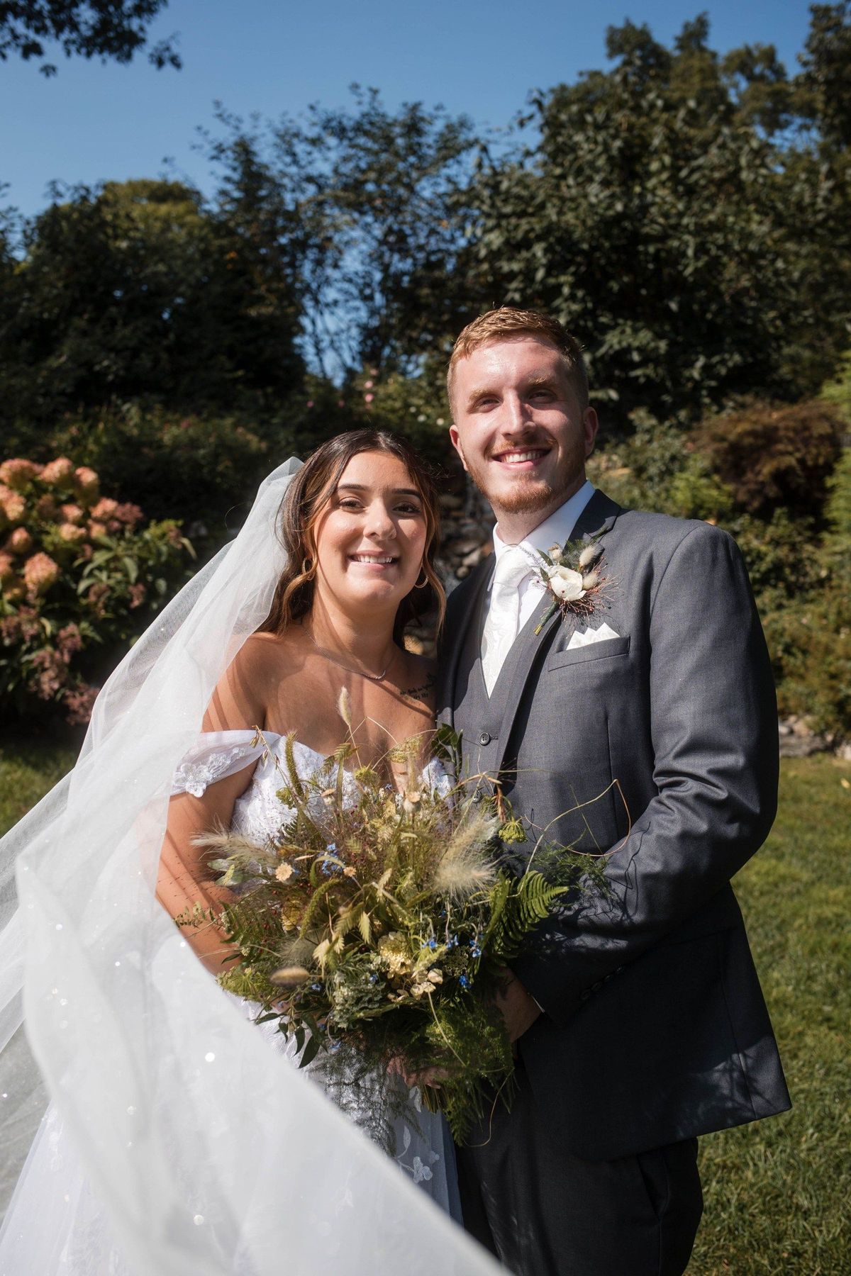 Sophia and Tommy smile together in the garden with her bouquet