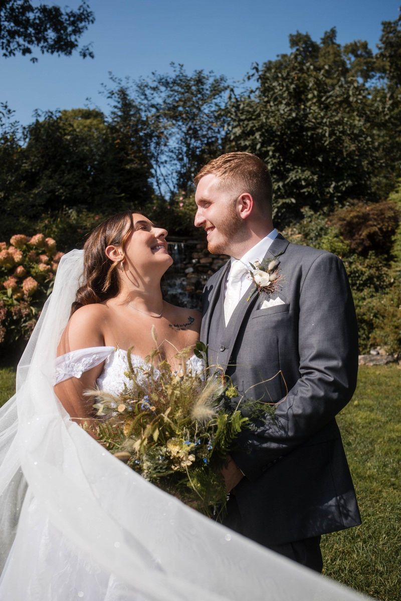 Sophia and Tommy look at one another while holding her bouquet in the garden