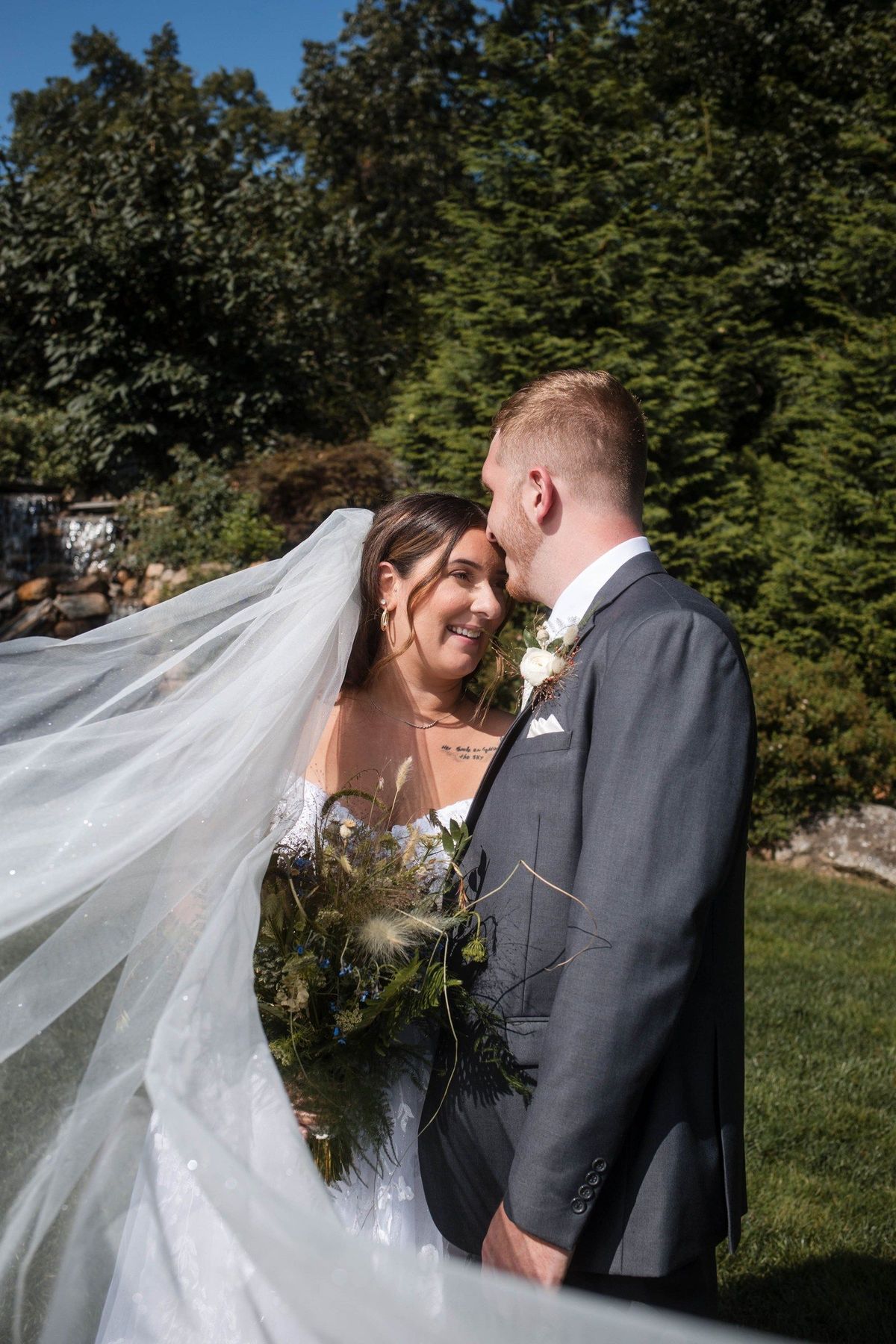 Tommy kisses Sophia on the forehead as her veil sweeps across the garden portrait