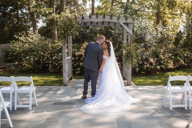 Sophia and Tommy embrace beneath the garden arbor in a wide portrait