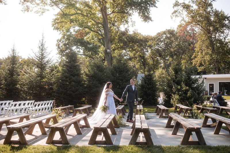 Sophia and Tommy walk hand in hand between empty ceremony benches, seen from the side in the garden