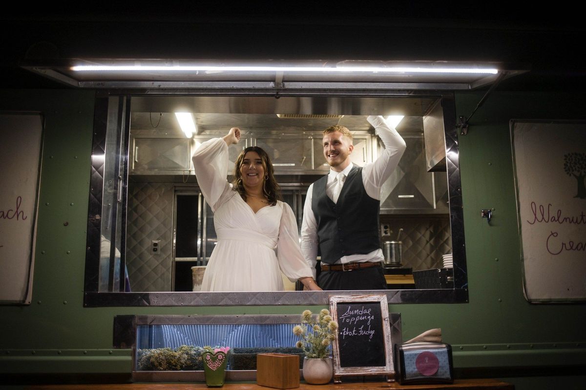 Sophia and Tommy raise their arms at a food truck serving window at night