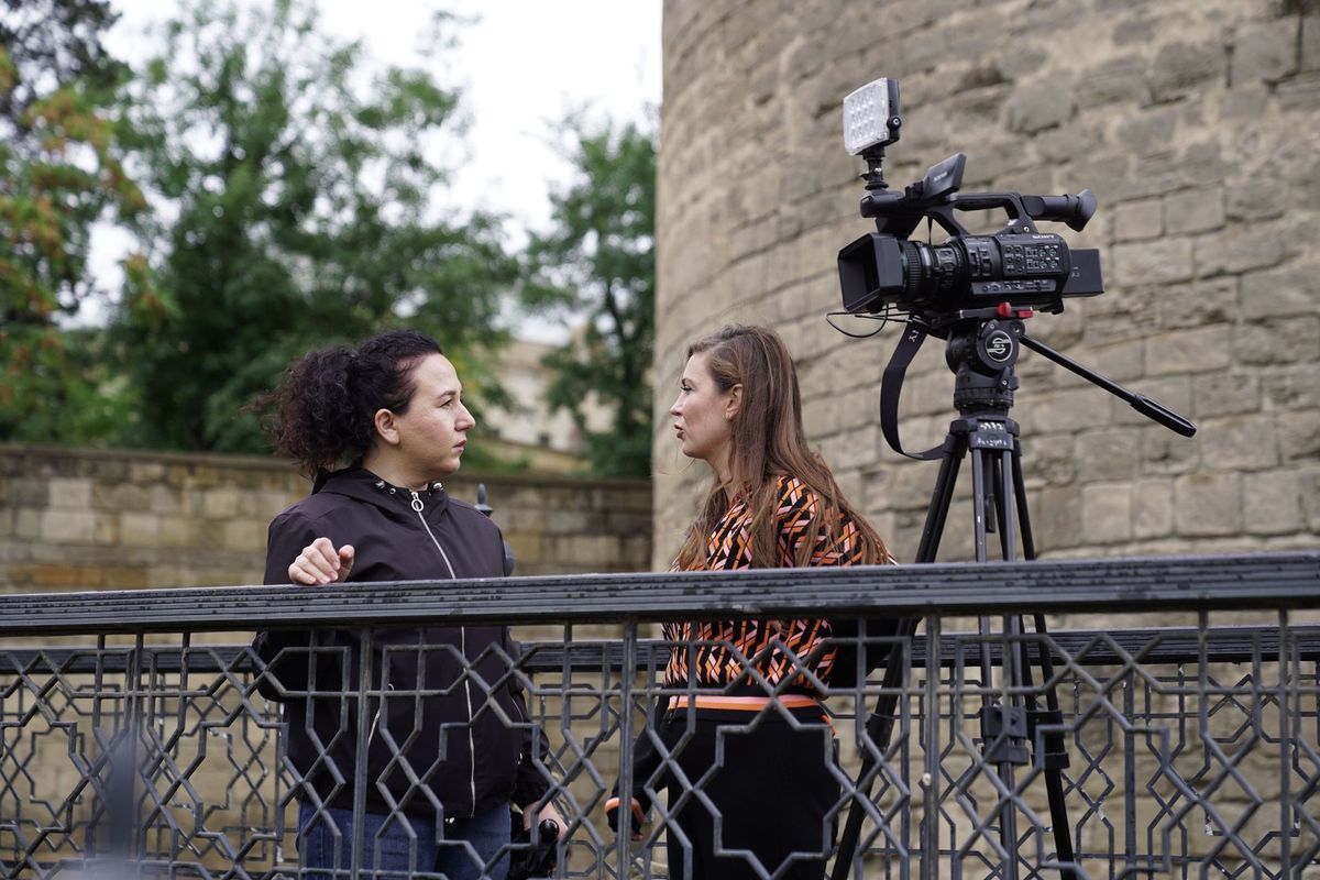 Two women in an outdoor interview with a camera set up beside a historic wall