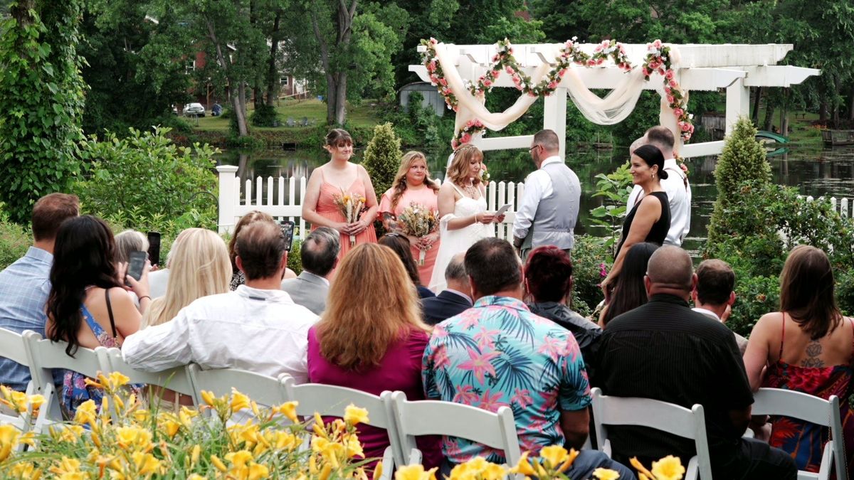 Wedding guests watch the ceremony beneath a draped pergola