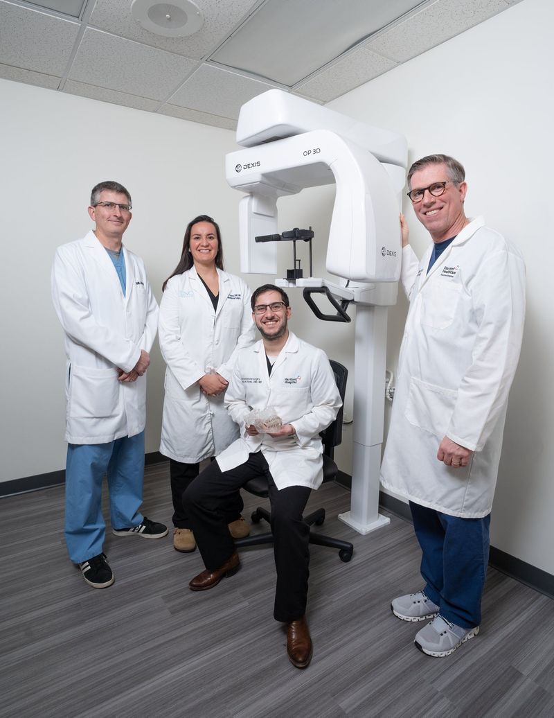 Four dental professionals in white coats posed together in a treatment room