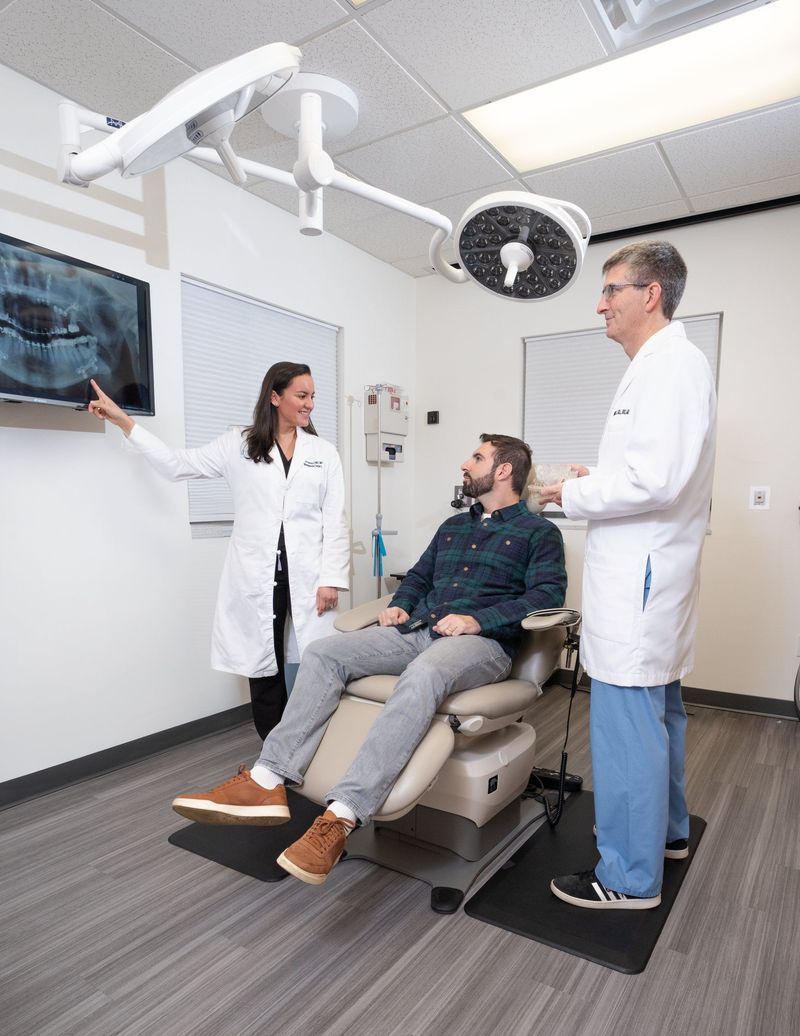Two dental professionals talking with a seated person in a treatment chair