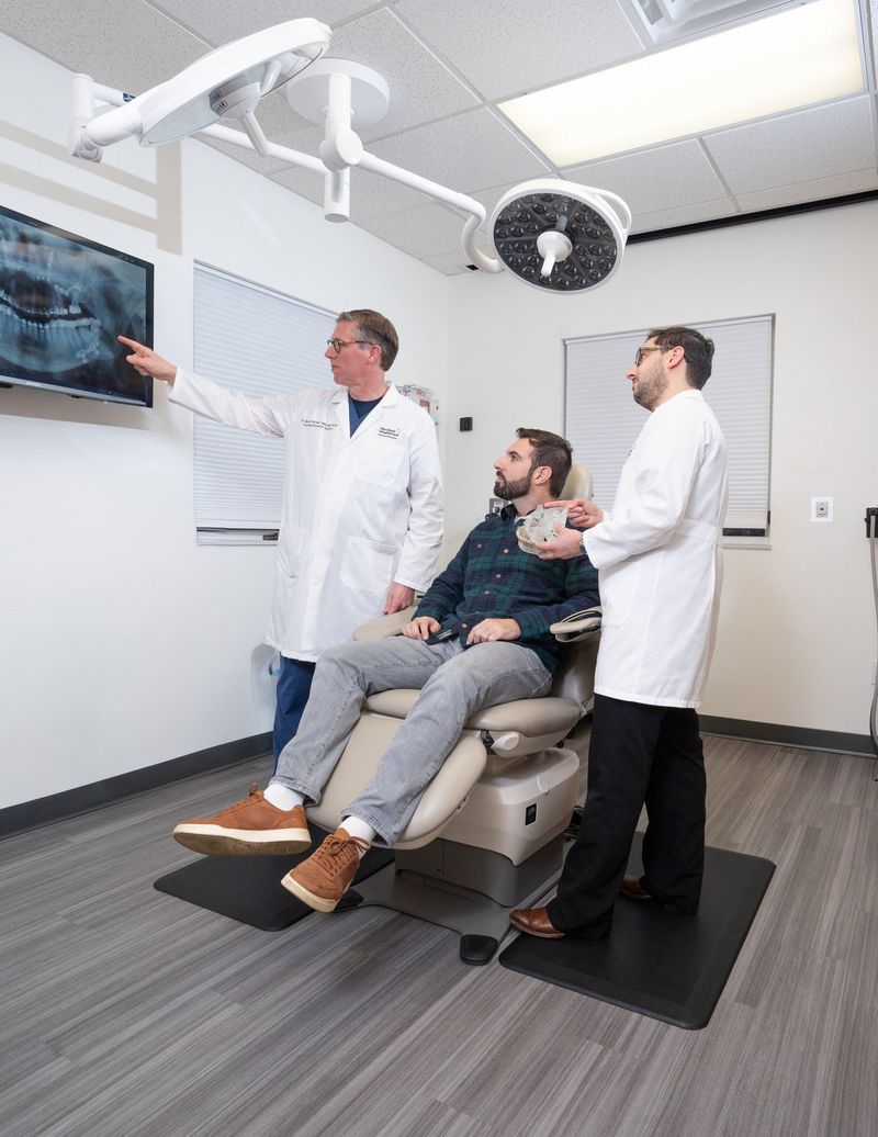 Dental professionals gesturing toward a screen beside a seated person