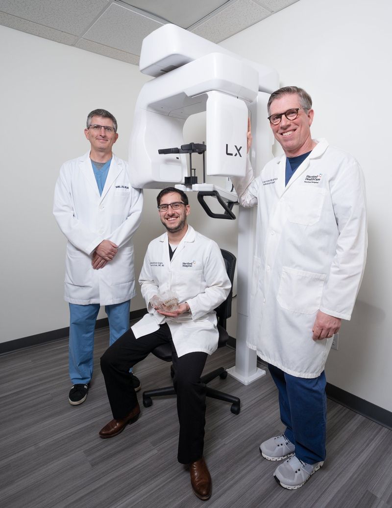 Three dental professionals posed beside clinical equipment