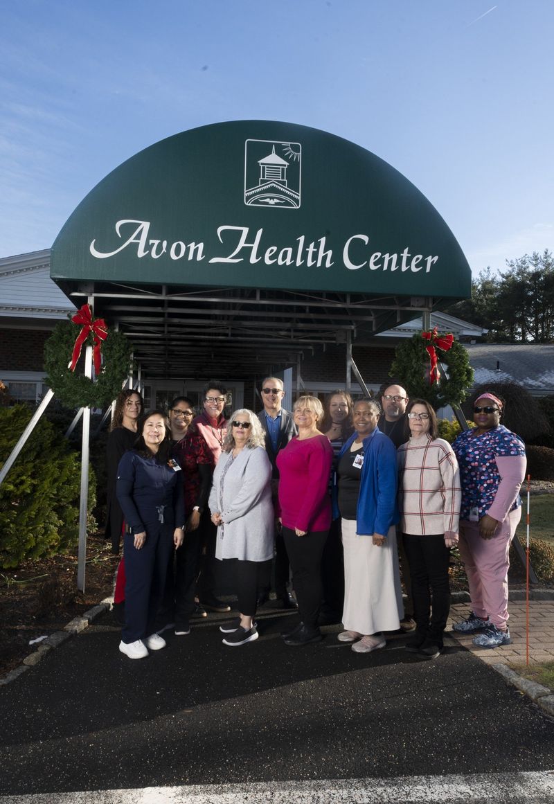 Team group portrait beneath the green Avon Health Center entrance awning