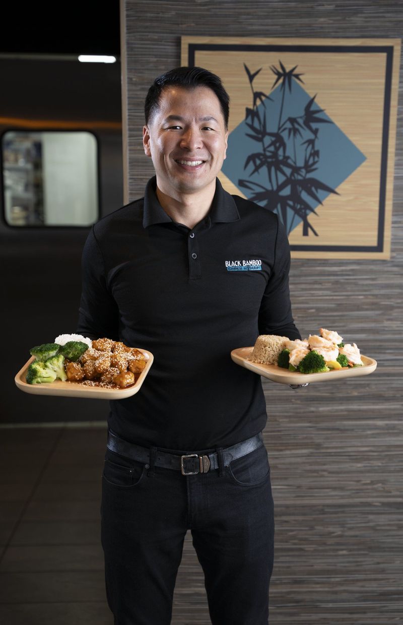 Smiling man holding two plates of food inside Black Bamboo