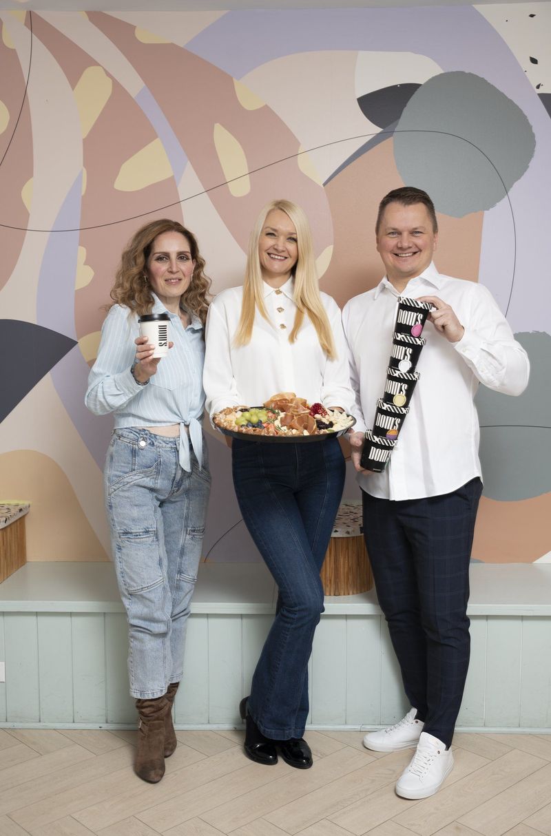 Full-length portrait of three people with drinks and a platter beside a pastel mural