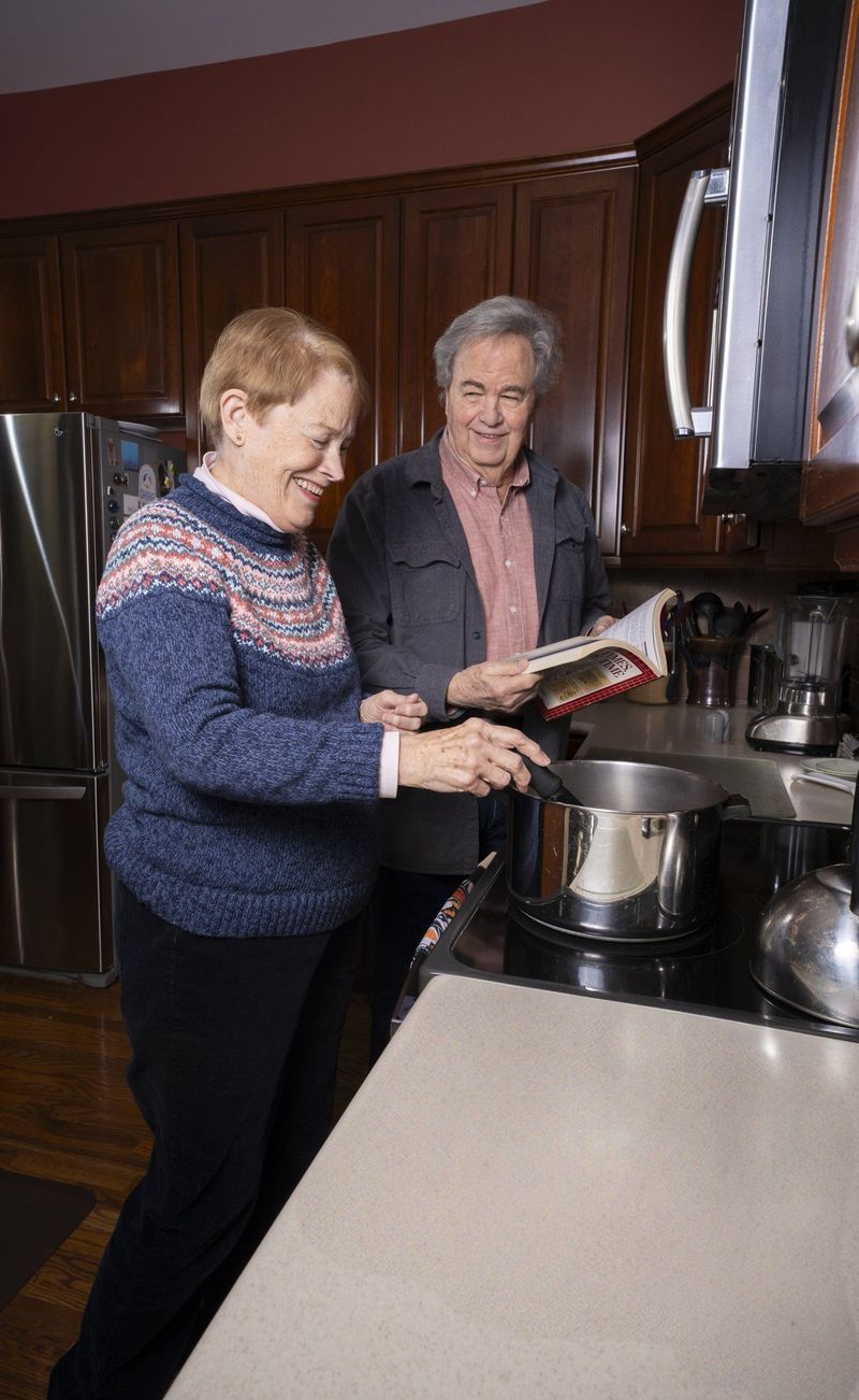 Two older adults together beside a pot on a kitchen stove