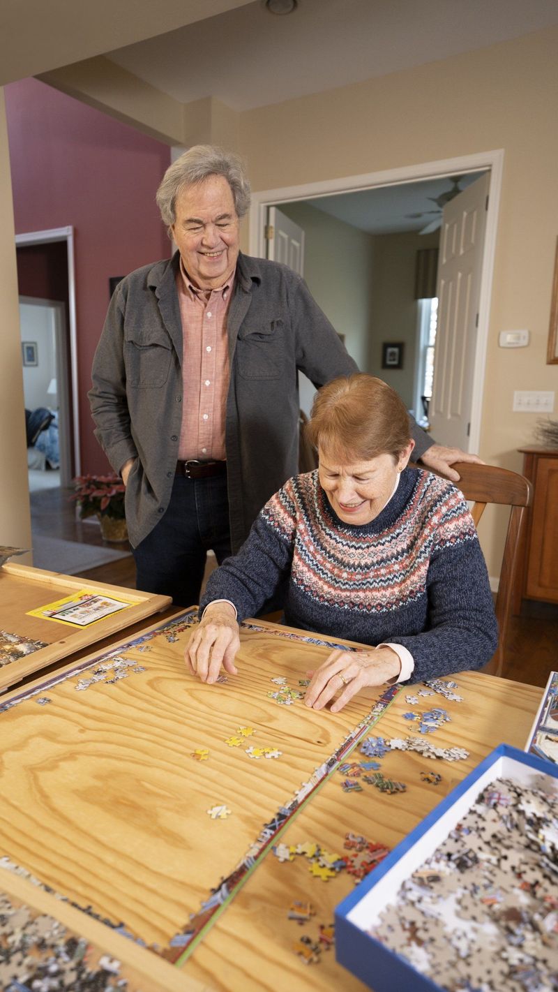 Older woman working on a jigsaw puzzle with a man standing beside her