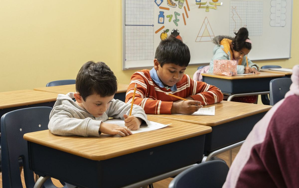 Students writing at classroom desks beneath a colorful mathematics display