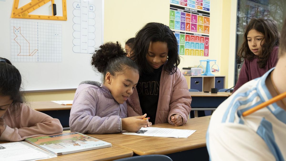Two students leaning over a workbook together