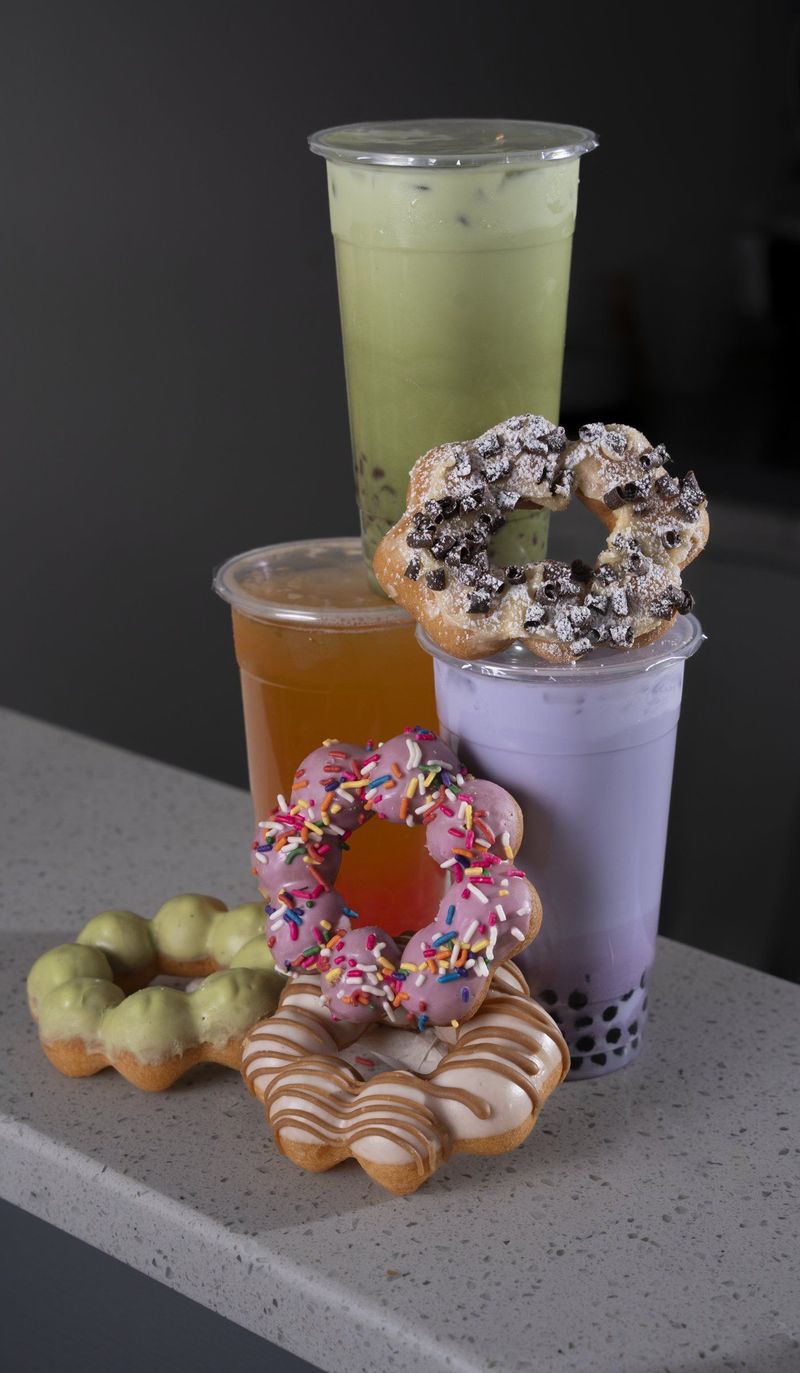 Colorful drinks and decorated mochi donuts arranged on a gray surface against a dark background