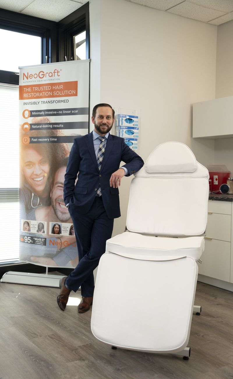 Man in a navy suit and patterned tie standing beside a treatment chair