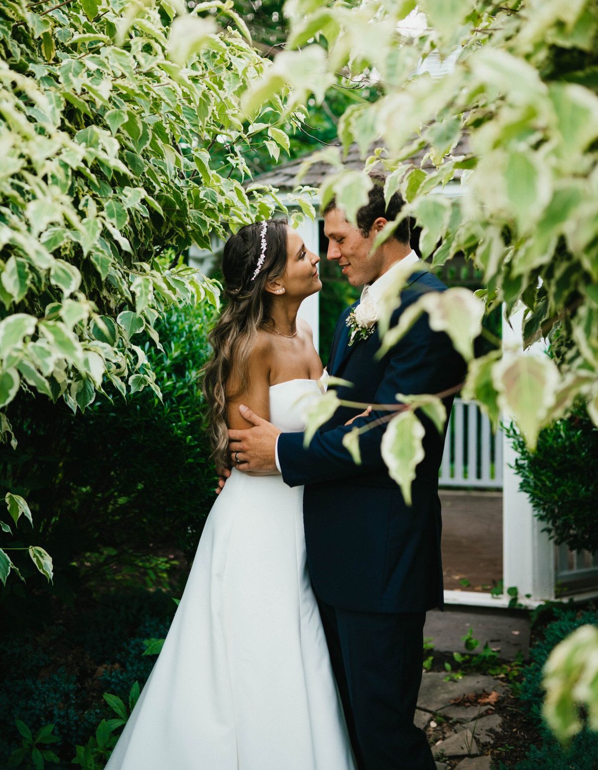 A bride and groom embracing and looking at each other, framed by green leaves