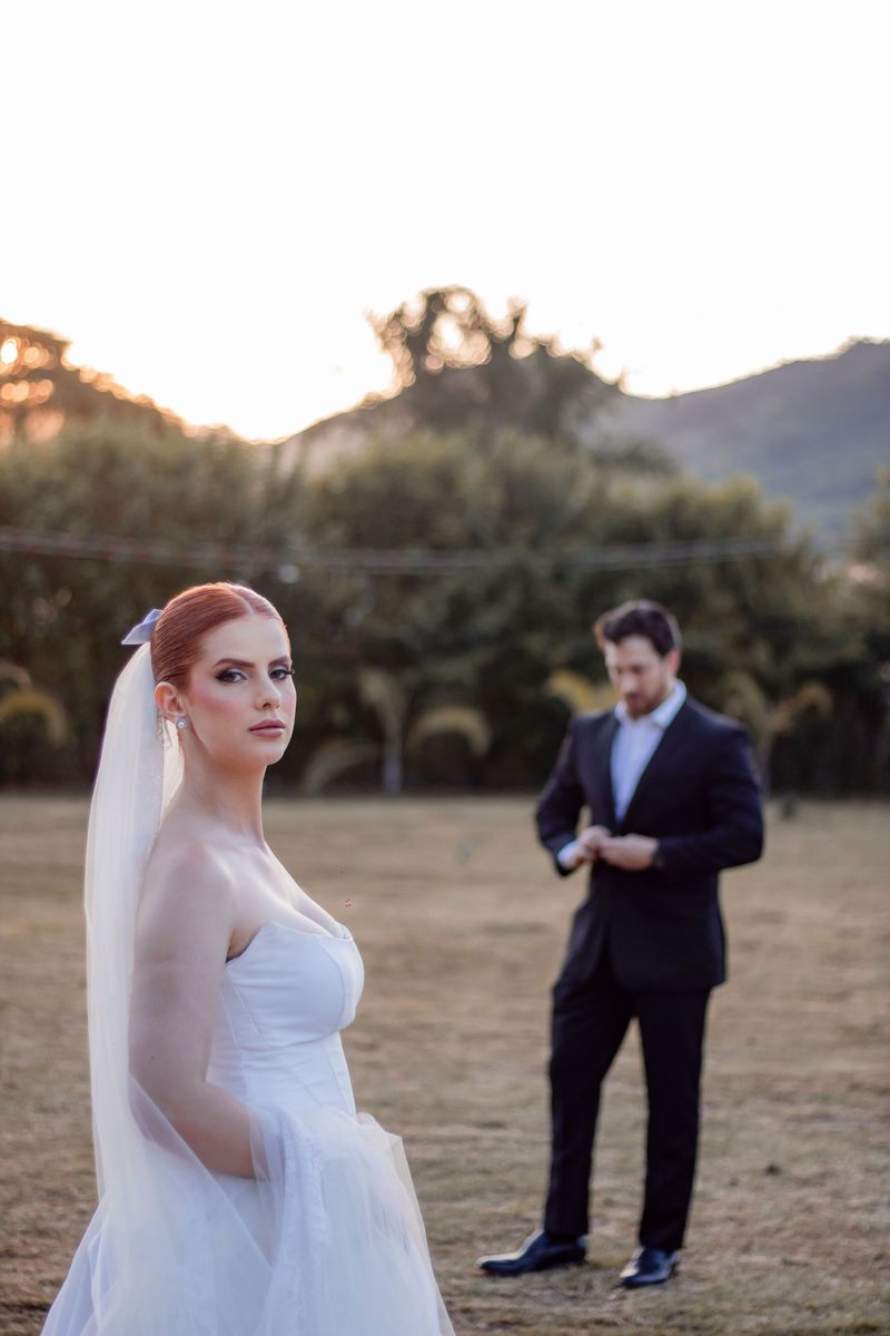 A red-haired bride in a veil looking at the camera while a groom in a dark suit adjusts his cuffs behind her