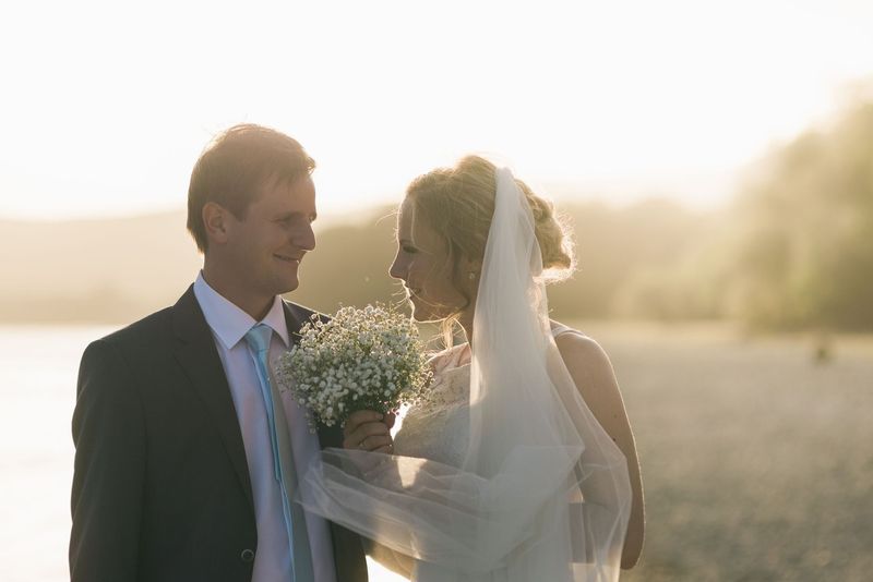 A smiling couple looking at each other in golden light, the bride in a veil holding a small bouquet of baby's breath