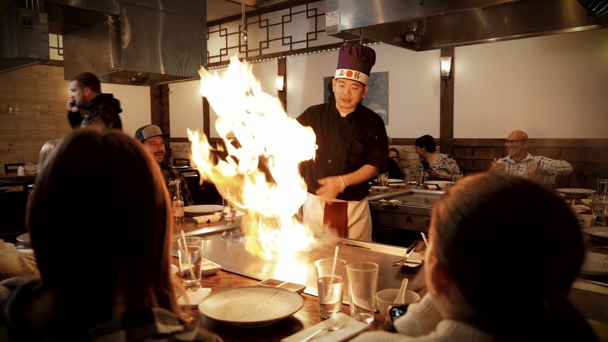 A Yume hibachi chef performs at the grill as flames rise before diners
