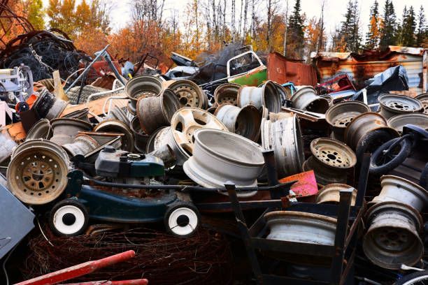 Pile of scrap metal auto parts and steel wheel rims at outdoor junkyard salvage recycling yard.
