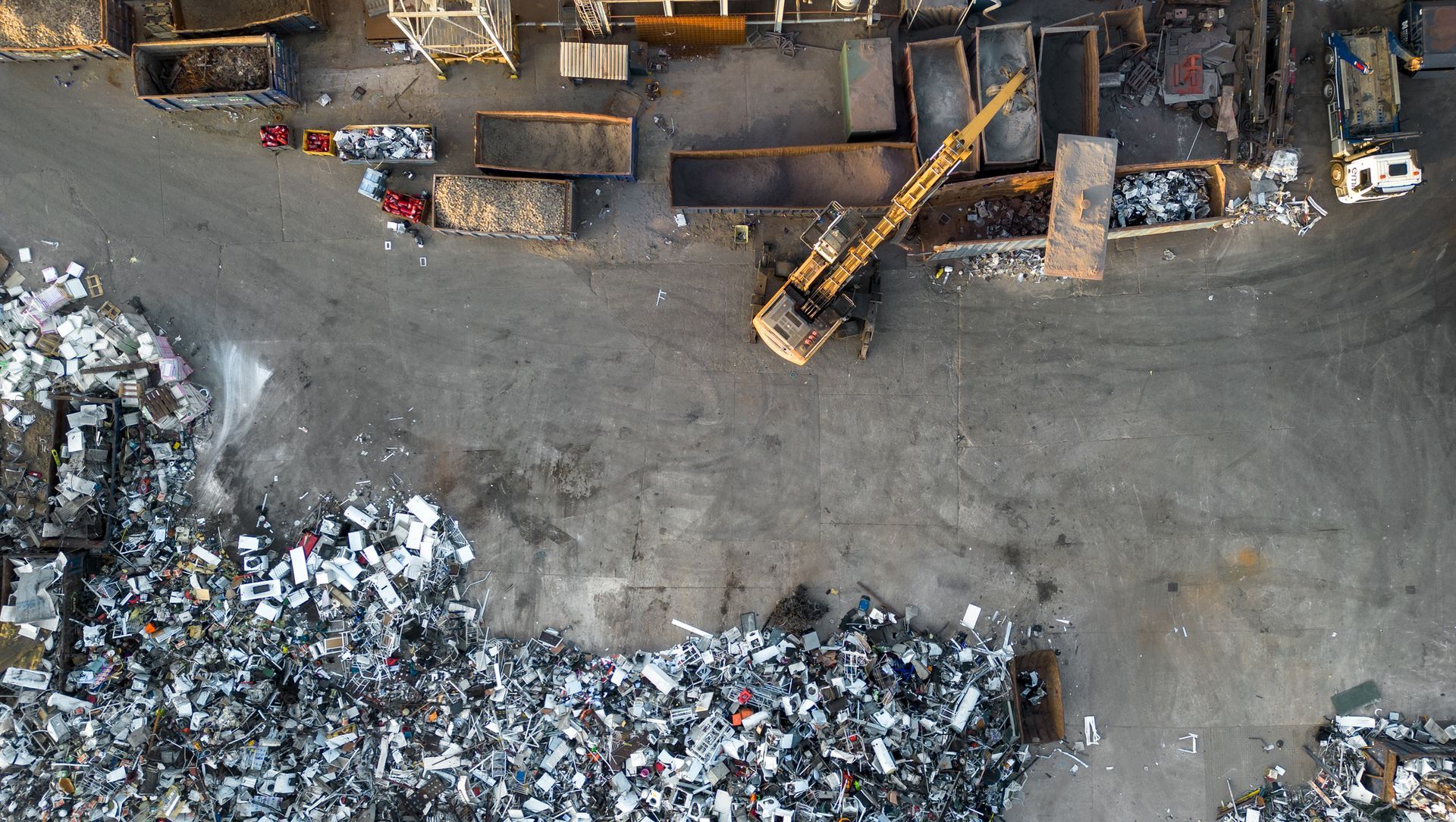 Overhead view of a junkyard with an excavator and piles of scrap metal.