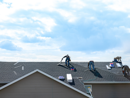 Workers installing solar panels on a gray shingled rooftop under a cloudy sky