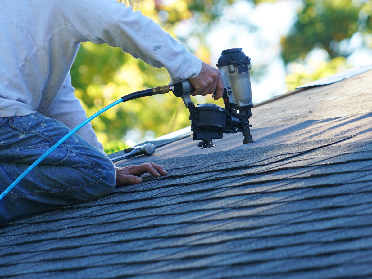 Worker using a pneumatic nail gun to install roofing shingles on a sloped roof