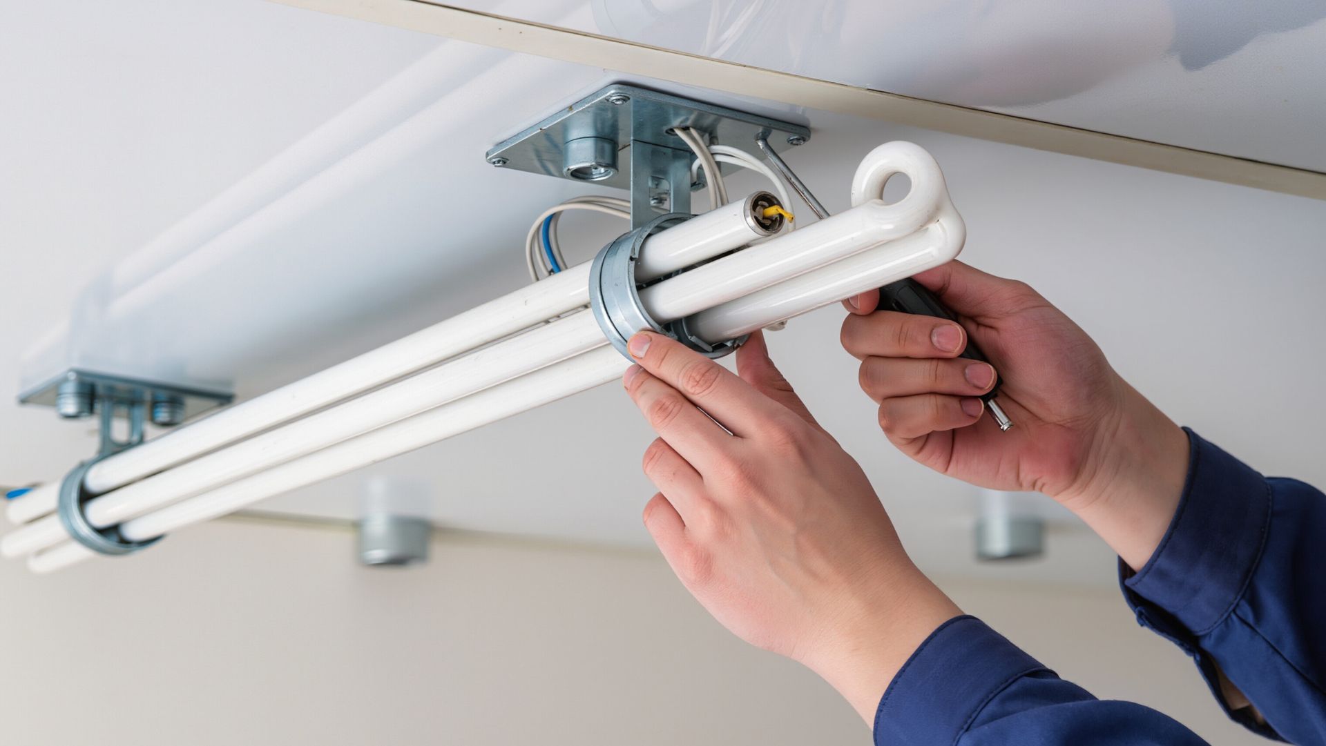 Person installing fluorescent light fixture on a white ceiling.