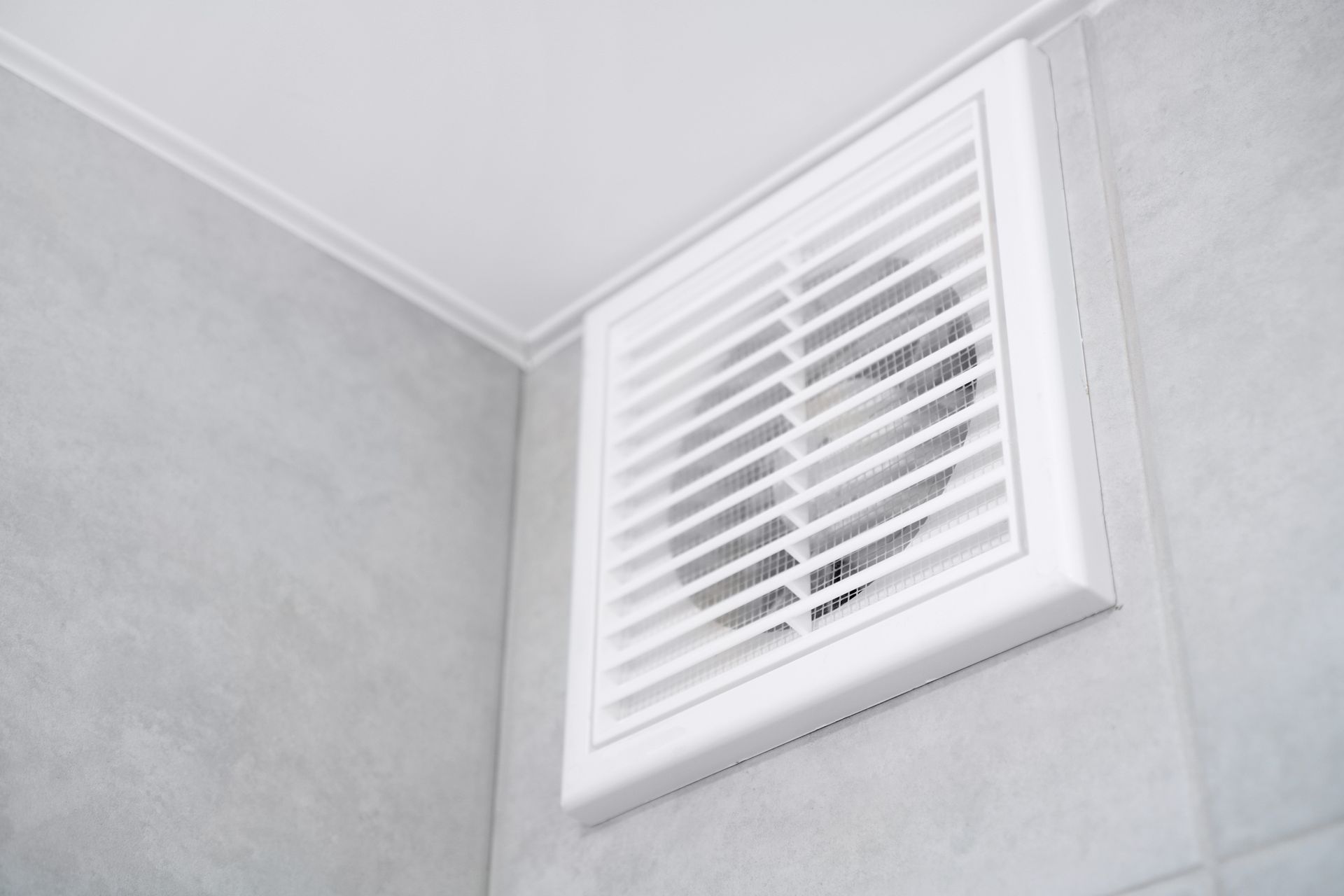 White bathroom vent on gray tile wall.