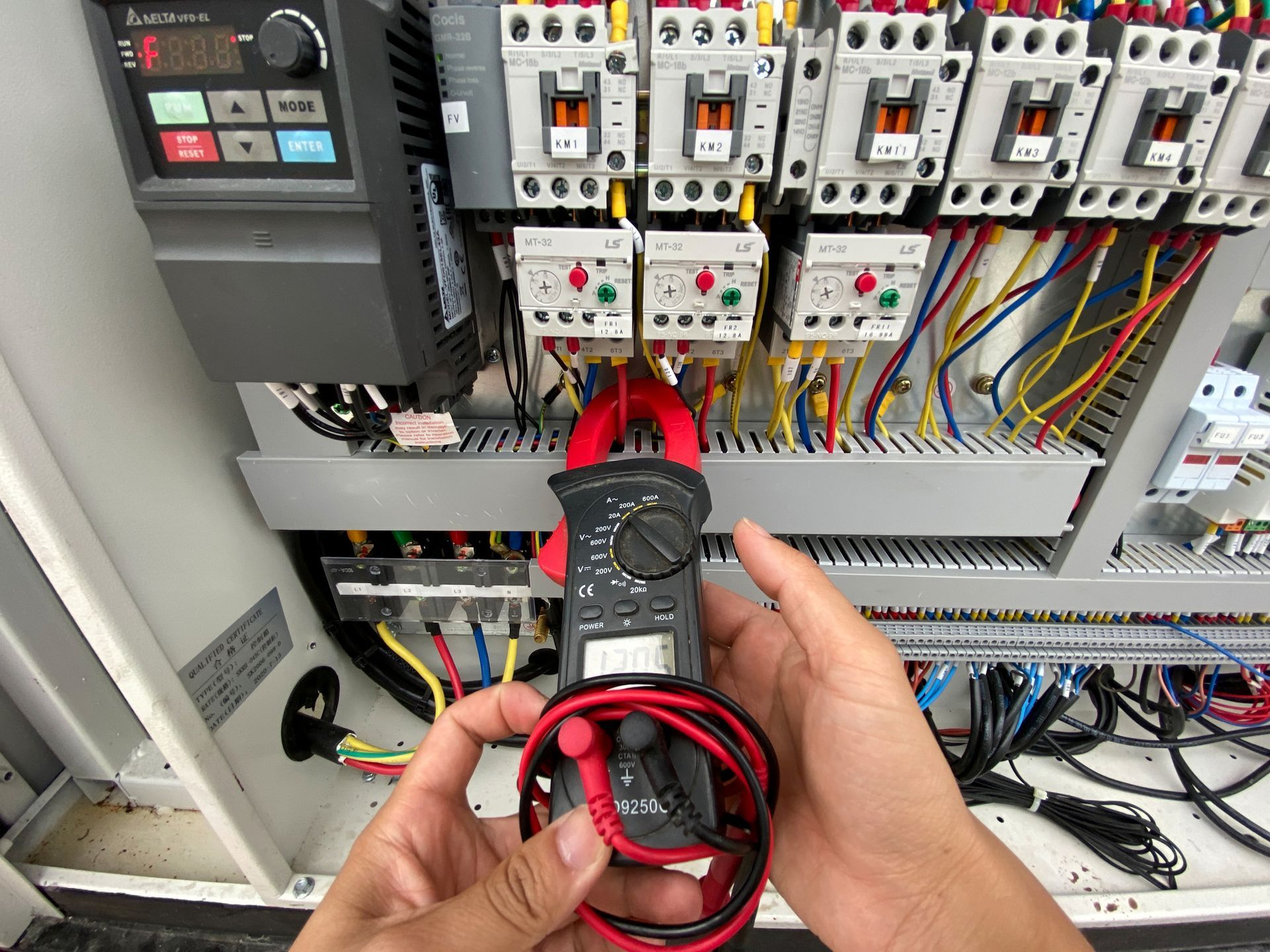 Person using a clamp meter to test electrical wires inside a control panel.