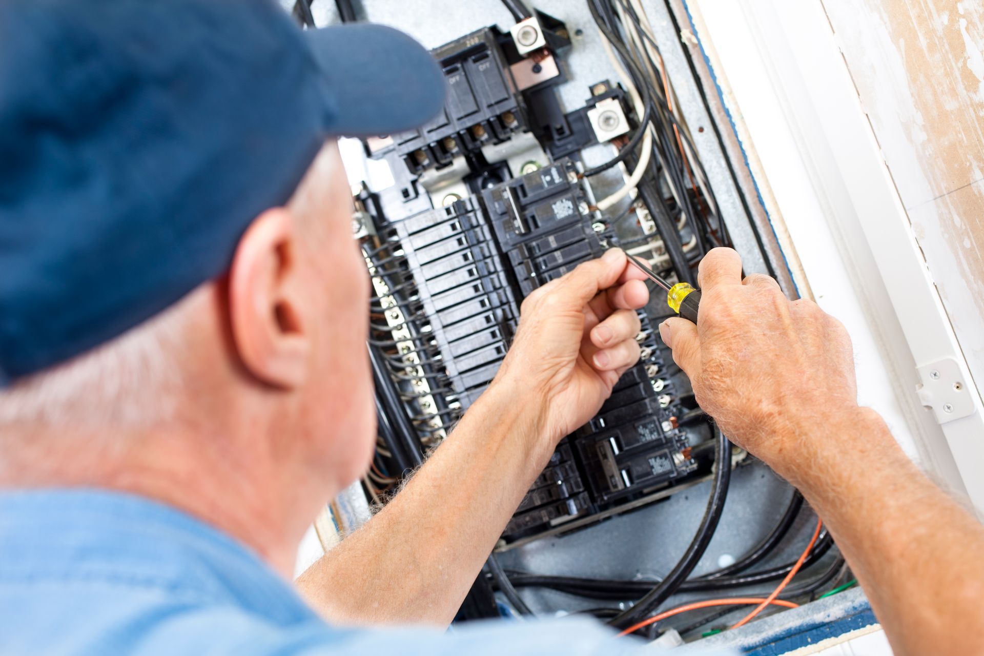 Electrician working on a circuit breaker panel with a screwdriver.