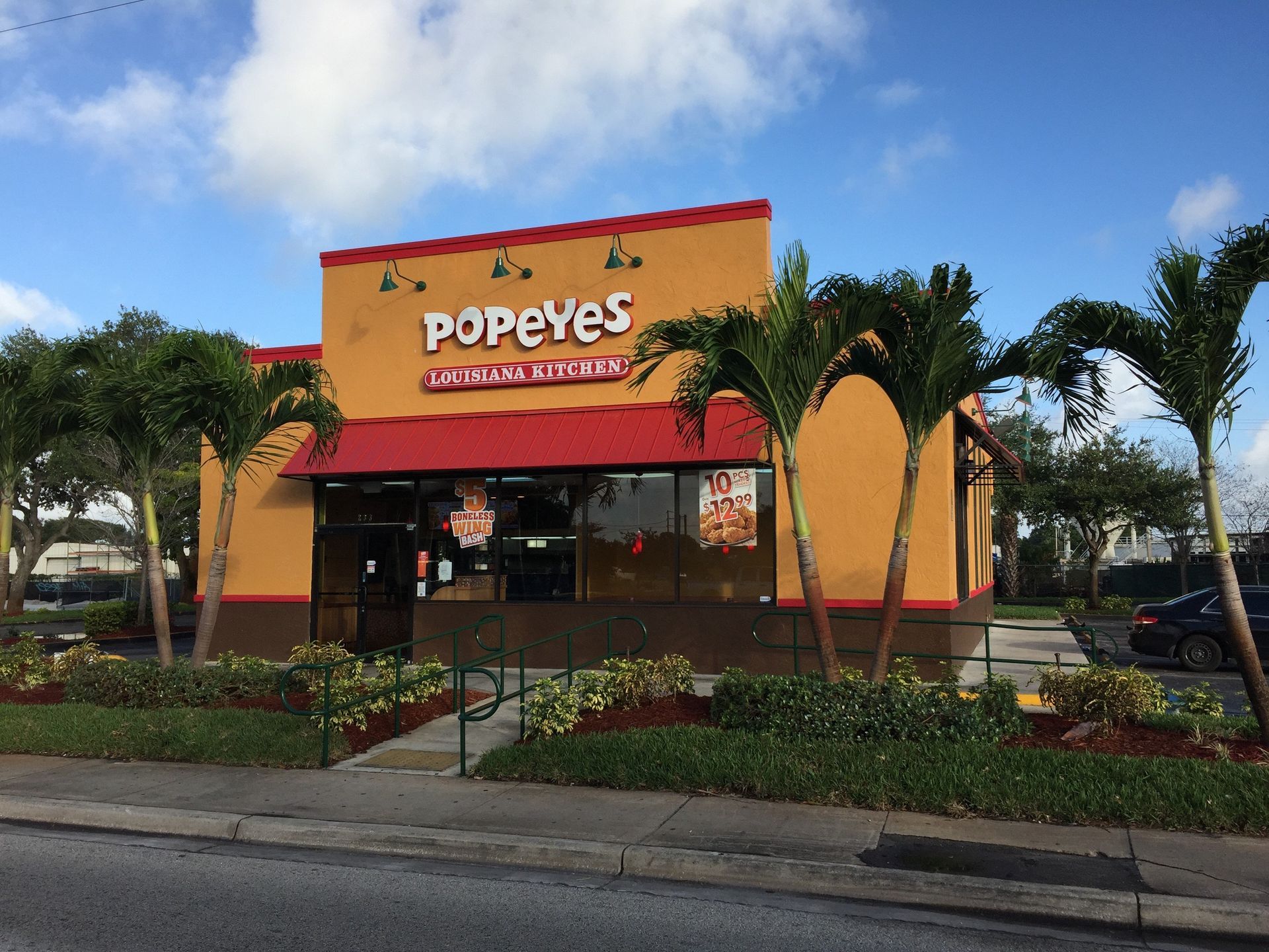 Popeyes restaurant with orange exterior and red trim. Palm trees in front.
