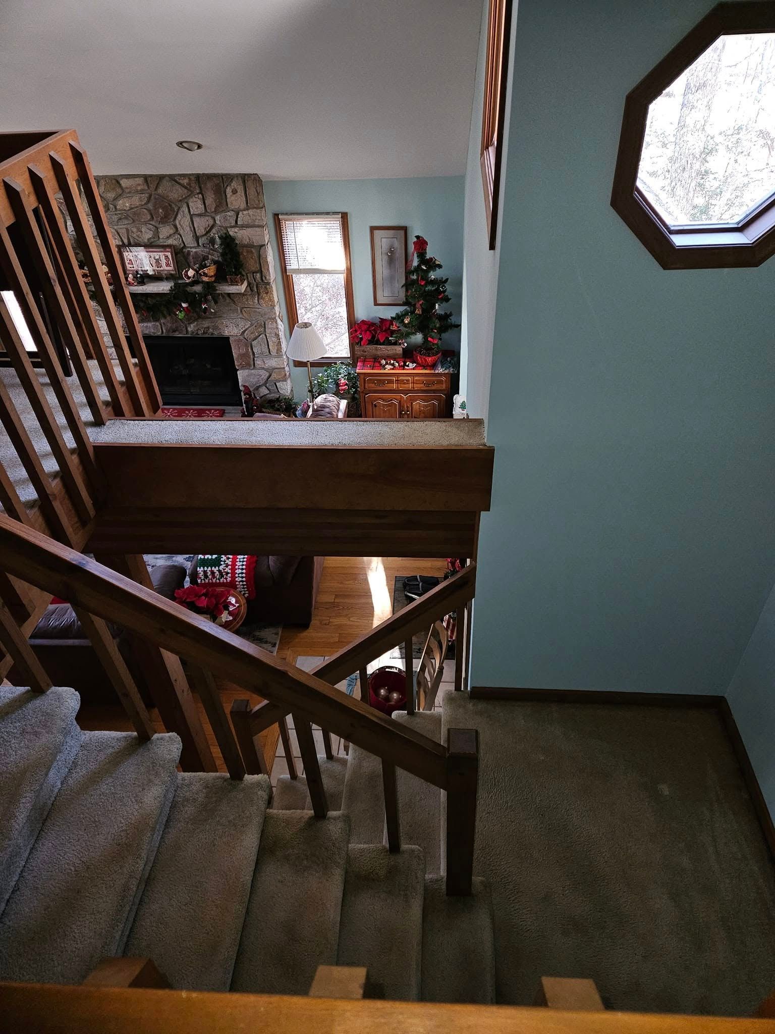 Staircase landing with wooden railings, carpeted steps, teal walls, and an octagonal window.