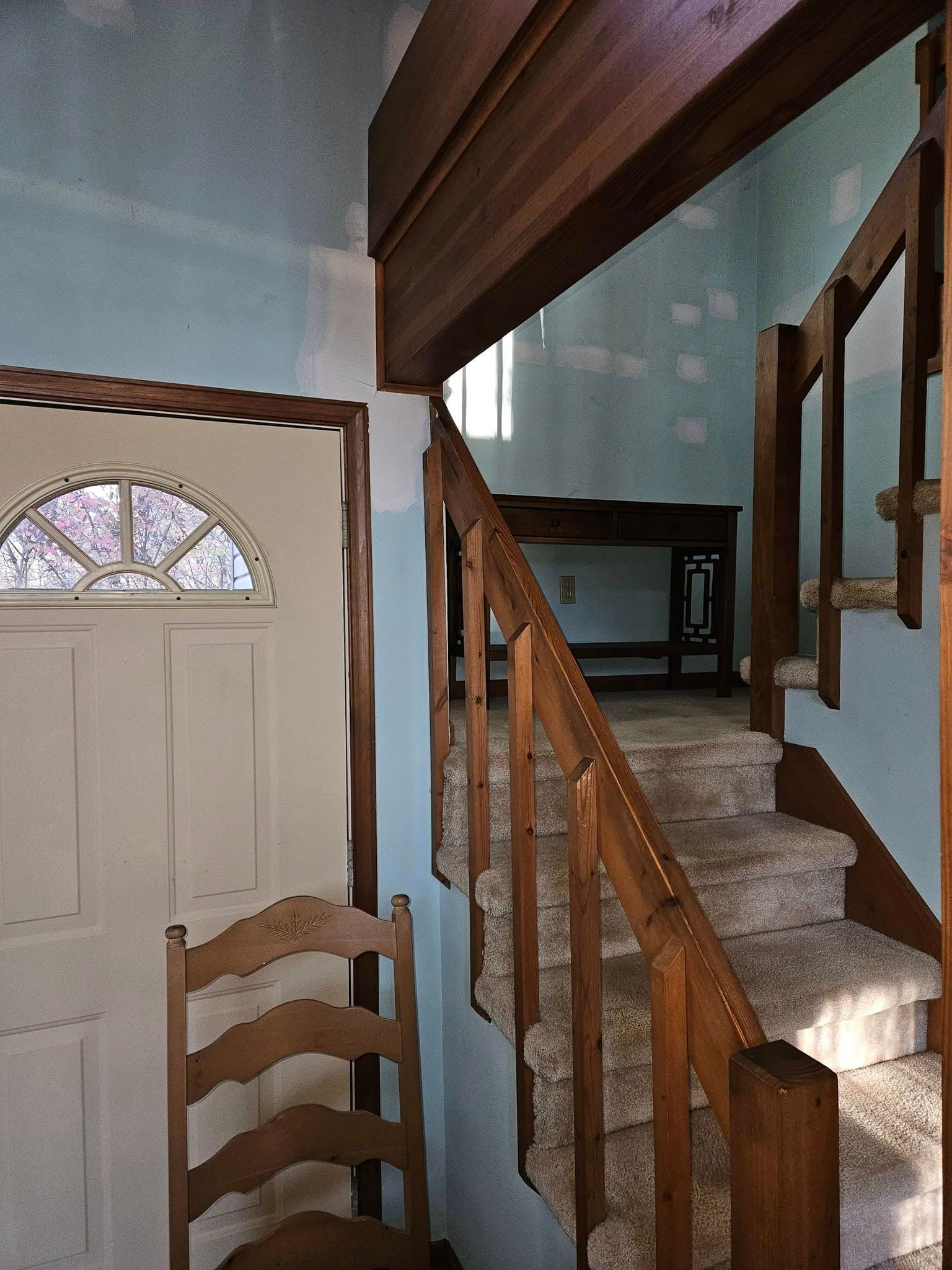 Interior entryway with staircase, wood railing, and front door with arched window panel