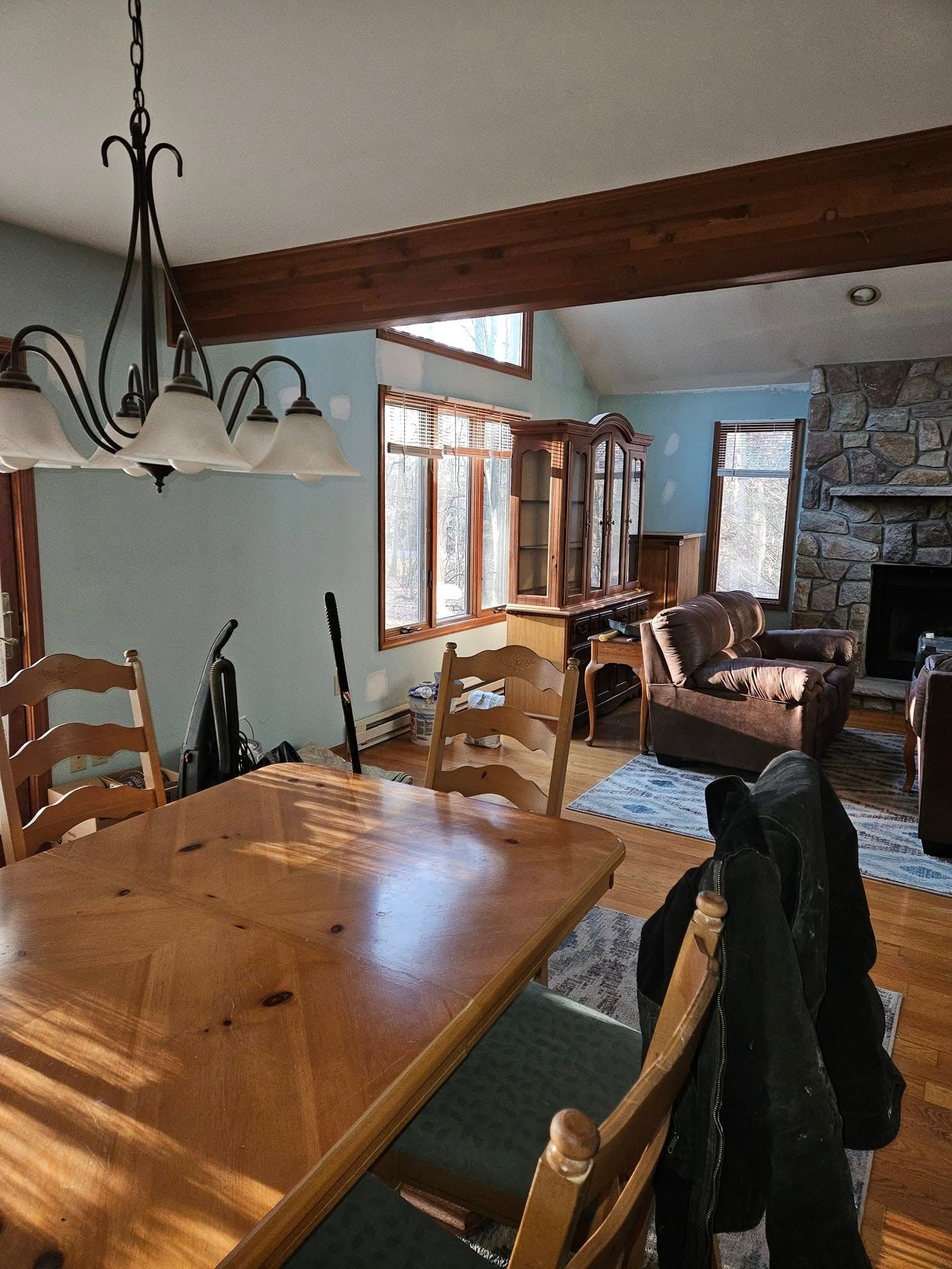 Wooden dining room with large windows, chandelier, and a stone fireplace in a rustic home