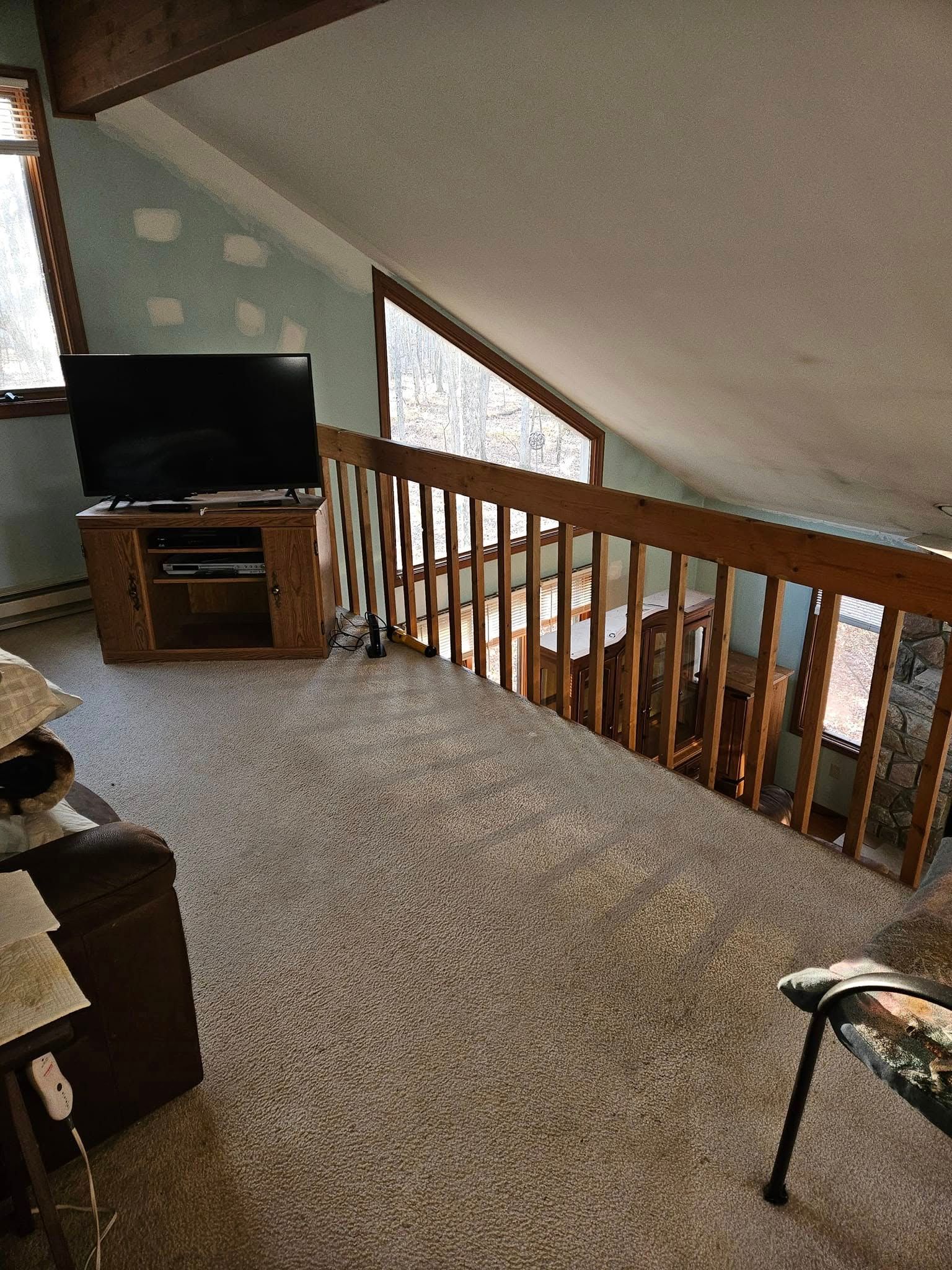 Loft living area with TV, wooden railing, and sloped ceiling with skylight windows.