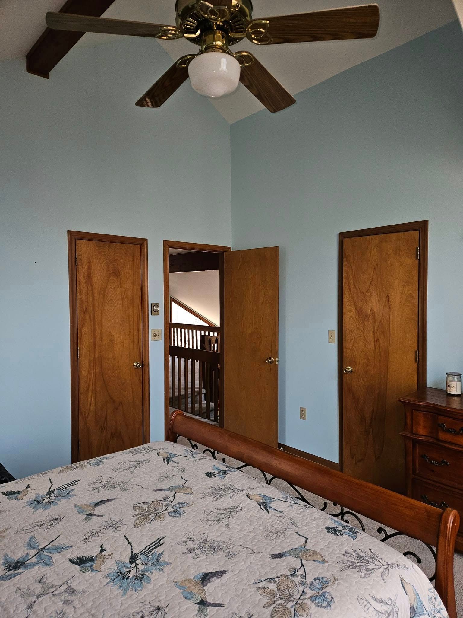 Bedroom with blue walls, bed in foreground, open doors to hallway, and ceiling fan overhead