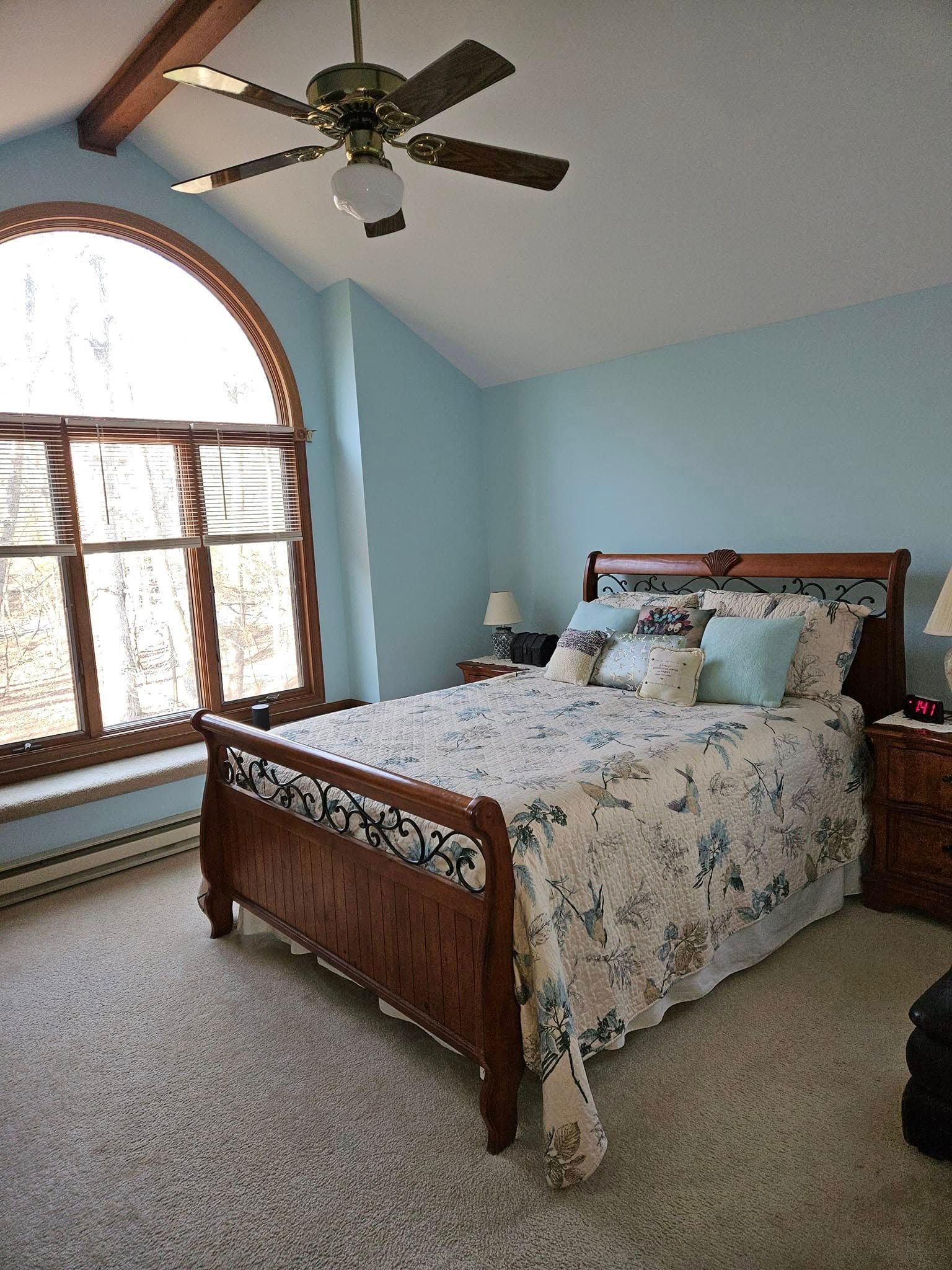 Bedroom with floral bedspread, arched window, and ceiling fan in a light blue room