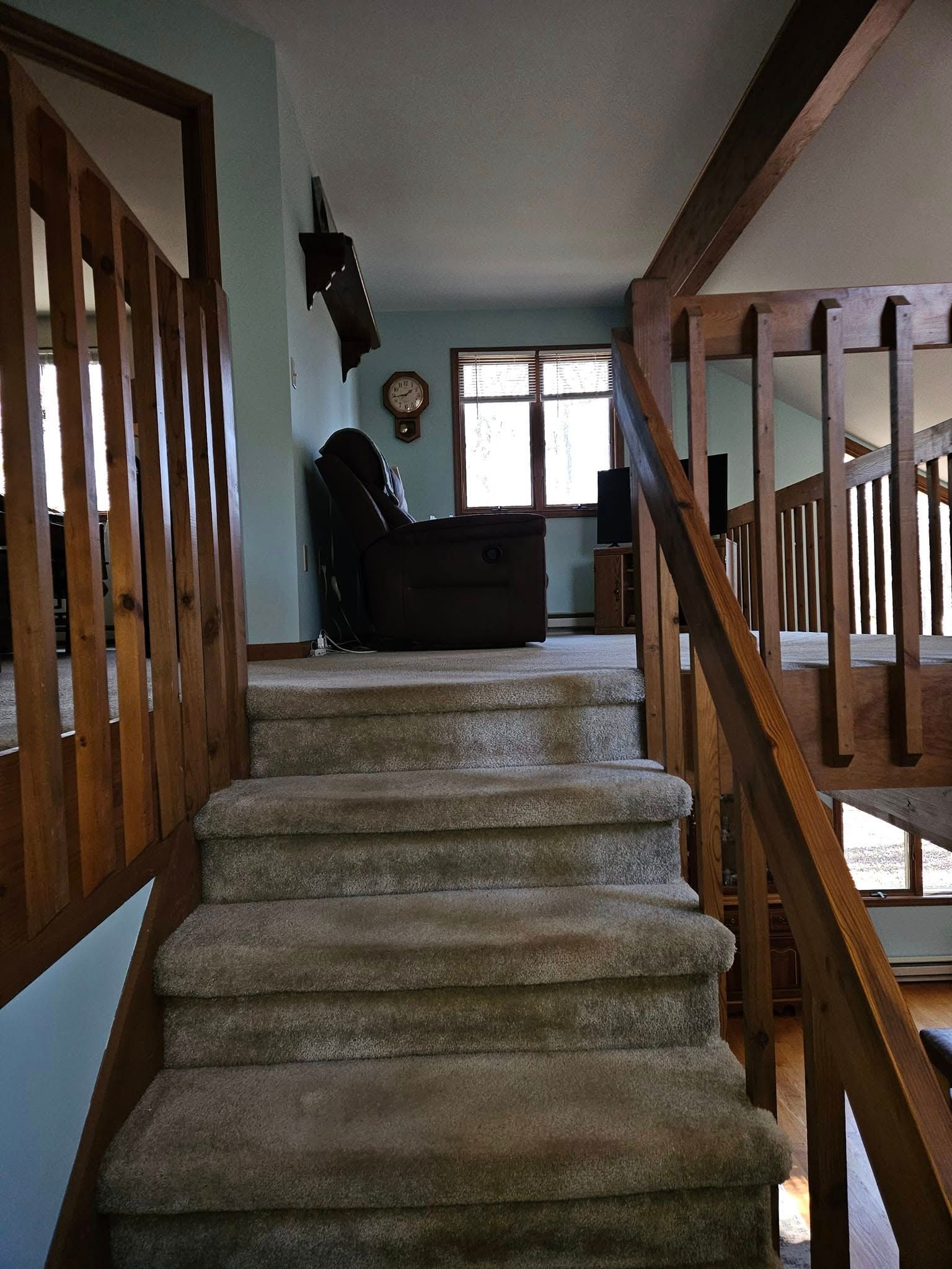 Carpeted staircase leading to a living room with a window and dark chair at the top