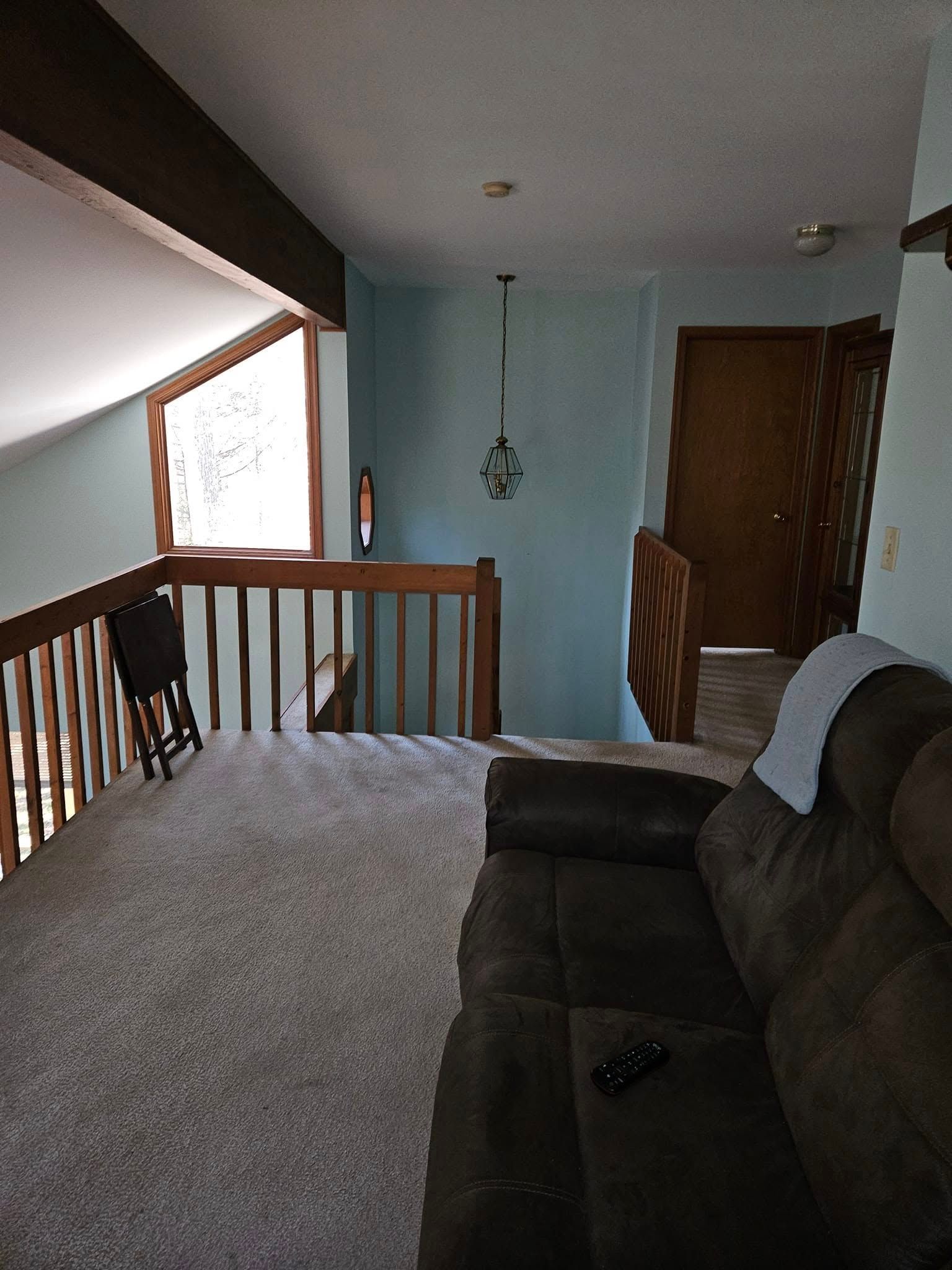 Upstairs living room with brown couch, carpeted loft, wooden railing, and blue wall leading to a hallway