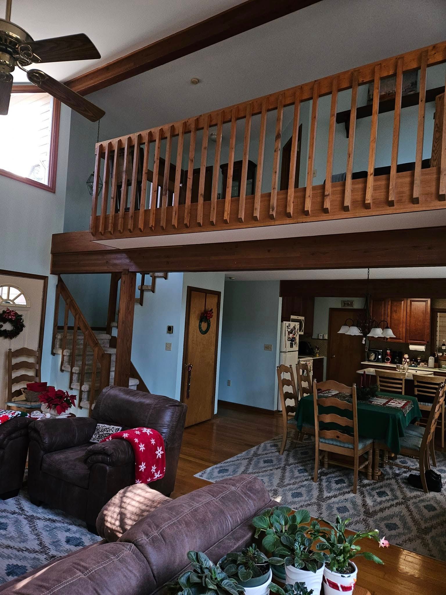 Loft-style living room with wood railing, leather sofas, patterned rug, dining area, and blue walls