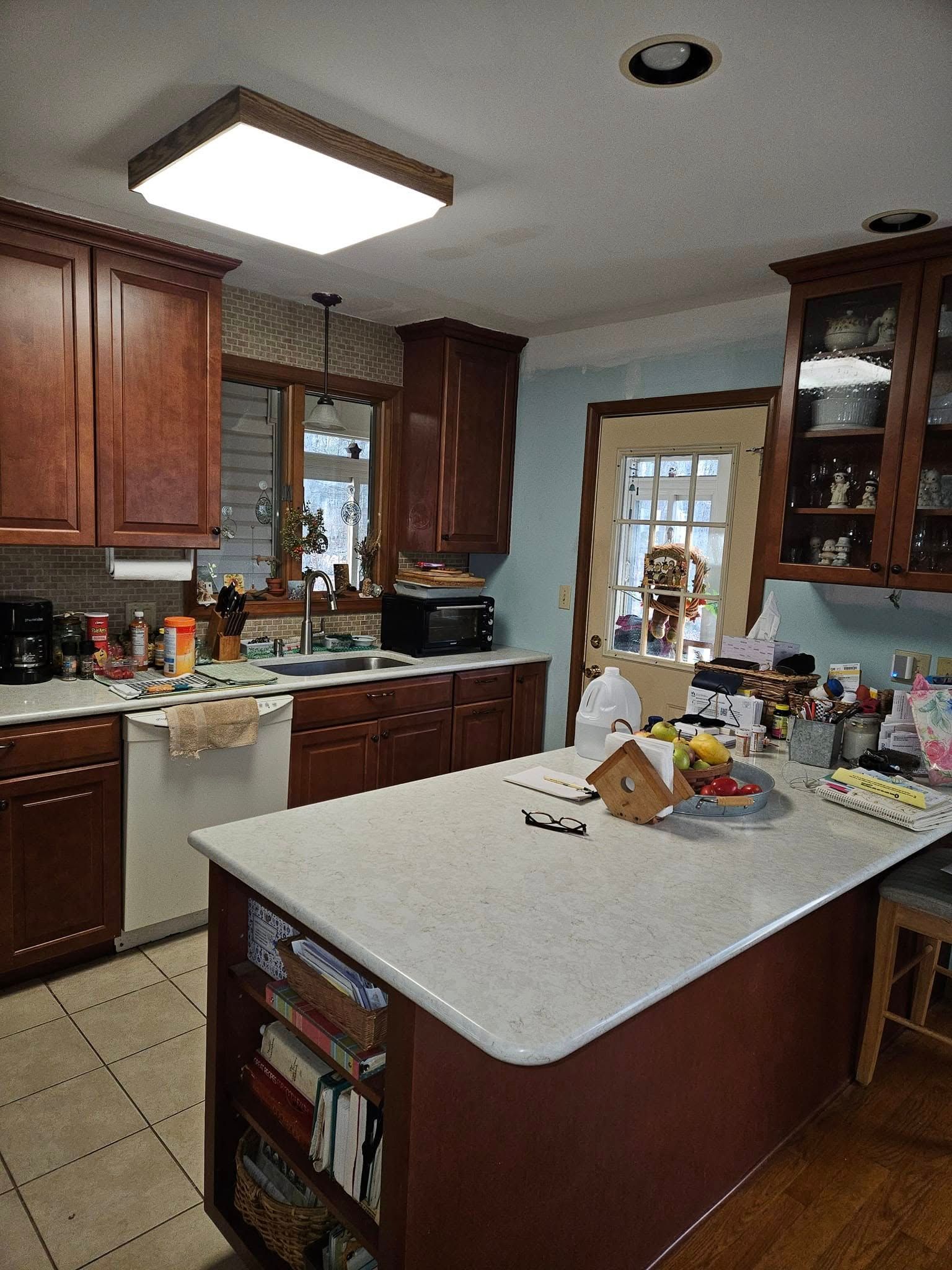 Kitchen with wooden cabinets, central island, and a bright ceiling light near a windowed back door.