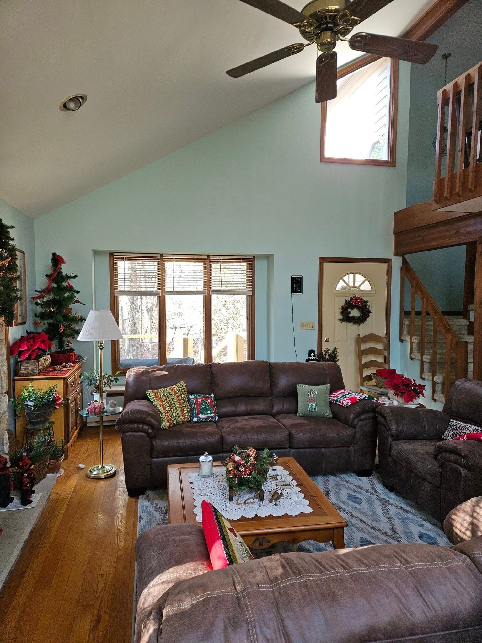 Cozy living room with leather sofas, a coffee table, staircase, Christmas tree, and vaulted ceiling fan