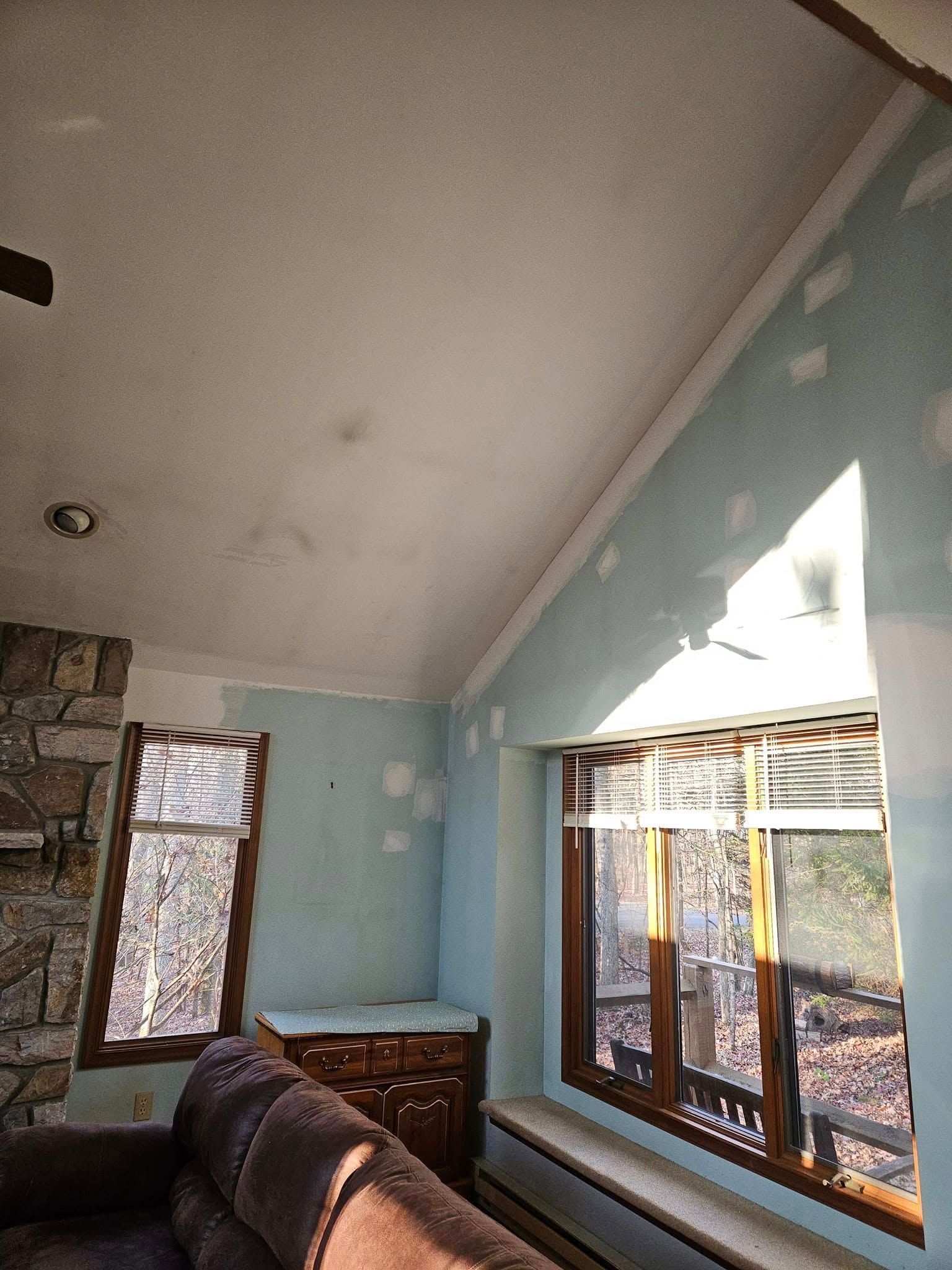 Living room with blue walls, large windows, and sunlight on a white ceiling; couch in foreground